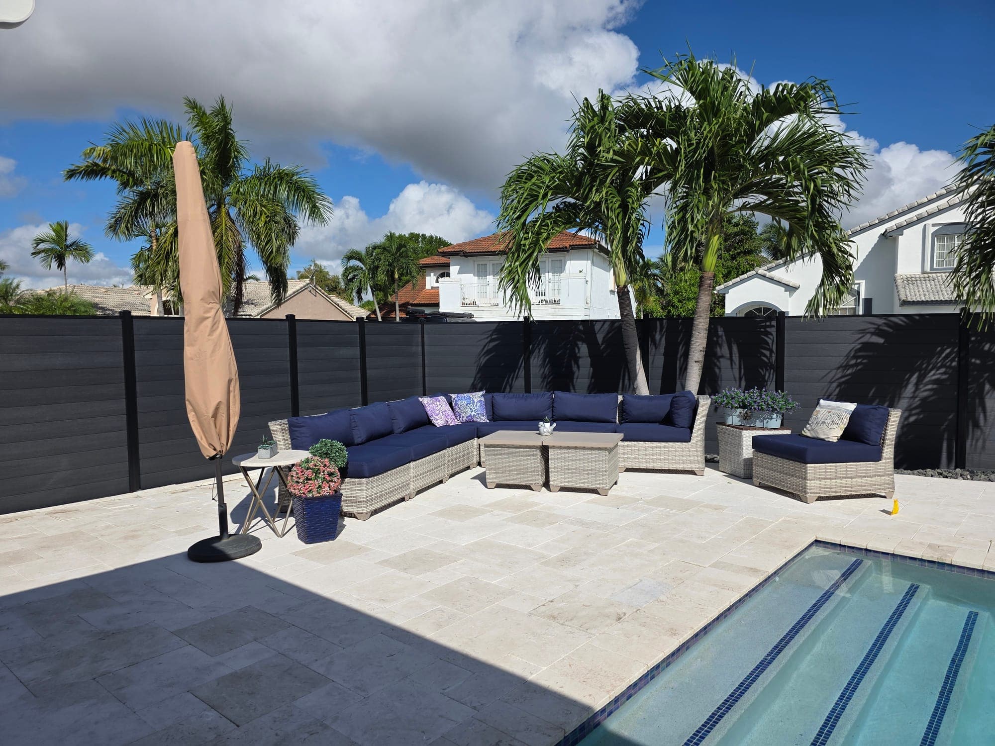 Black WPC privacy fence around a travertine pool patio