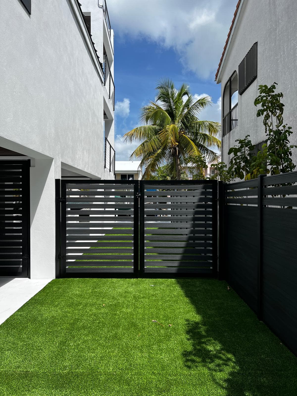 Black horizontal-slat WPC double gate and privacy fence beside a modern home