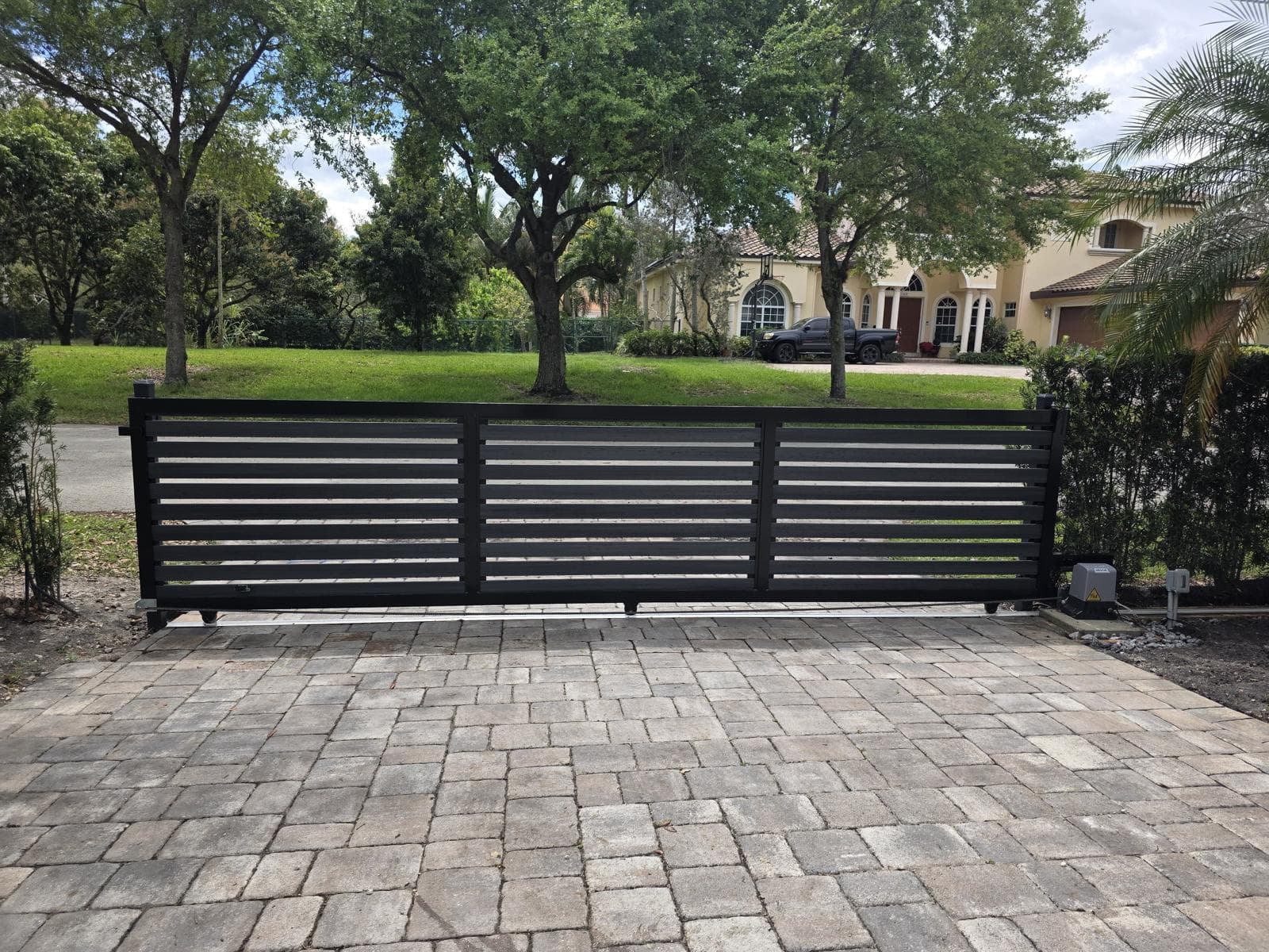 Black sliding driveway gate with horizontal WPC slats and an automatic opener